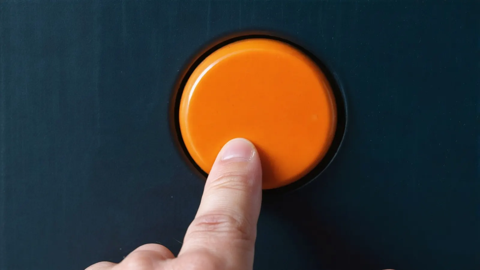 A finger pressing a large round orange button set in a dark navy panel
