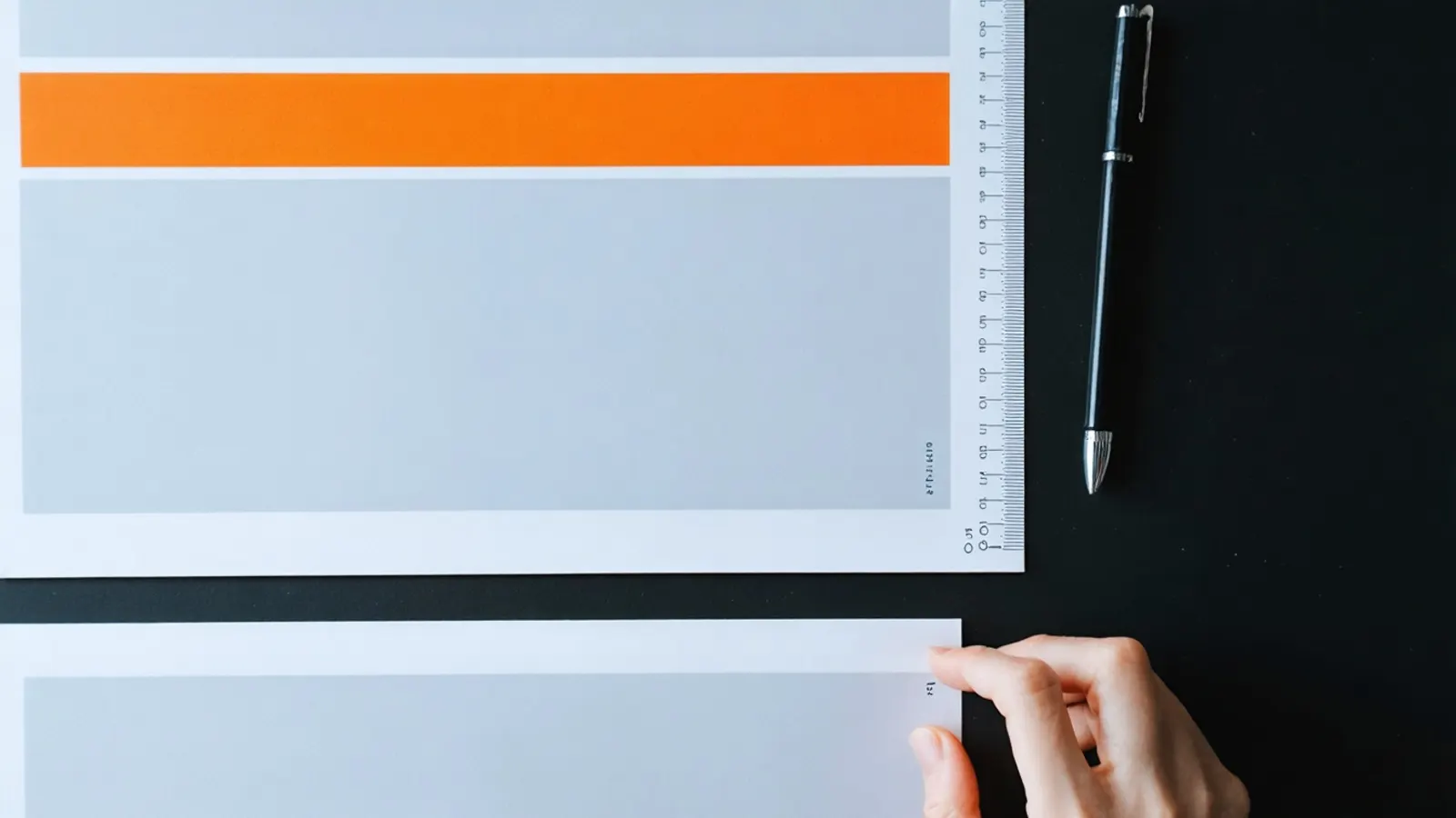 Two printed cards with matching orange bars beside a ruler and a pen