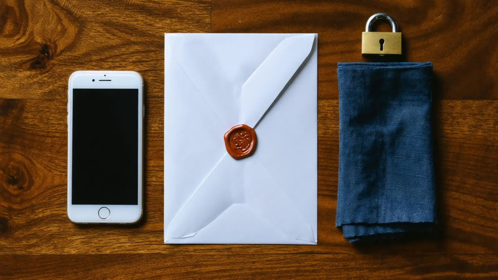 A phone, a sealed envelope and a padlock on a dark wooden table
